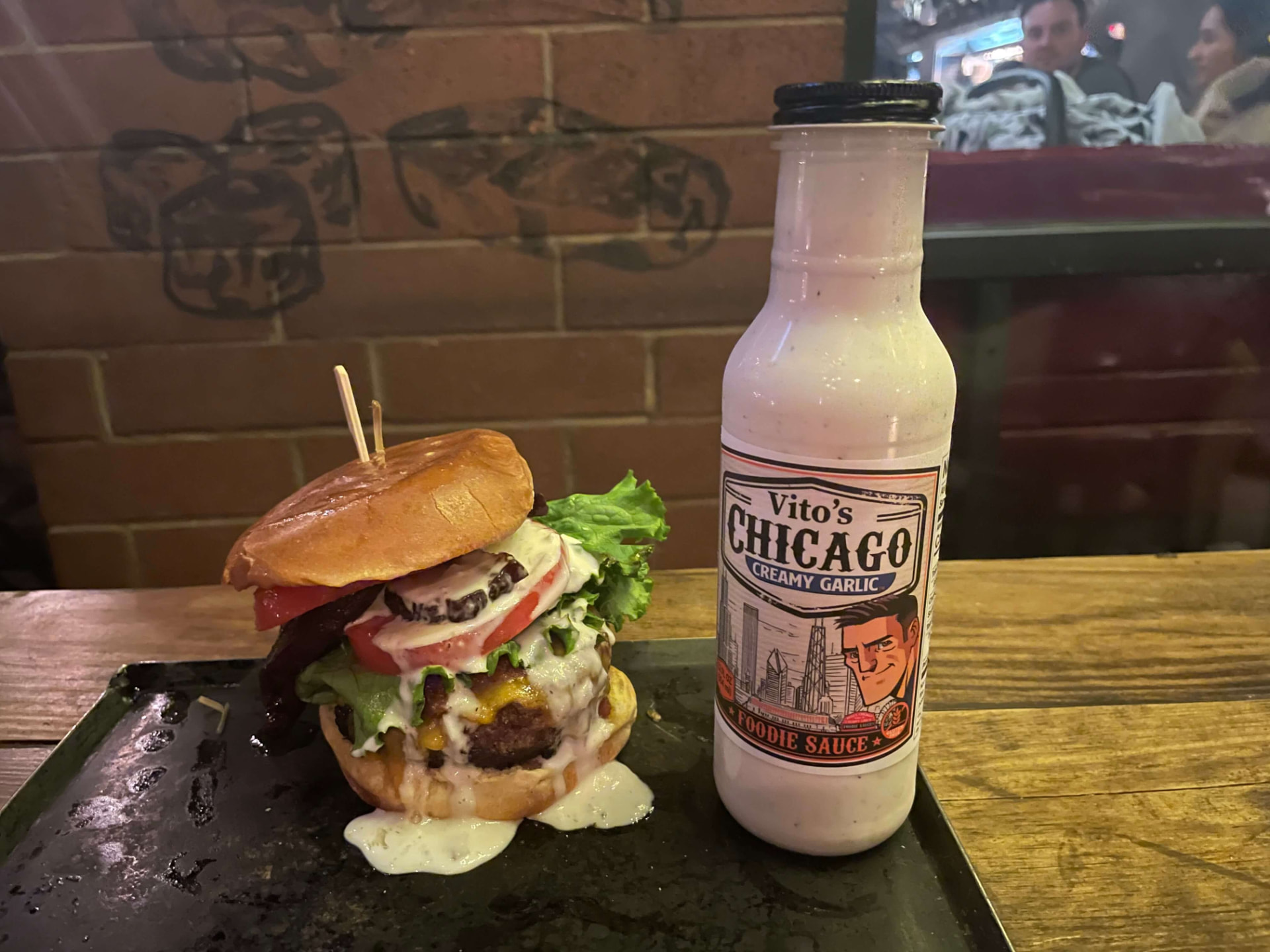 Stacked cheeseburger with sauce pouring down the bun next to a Foodie Sauce bottle