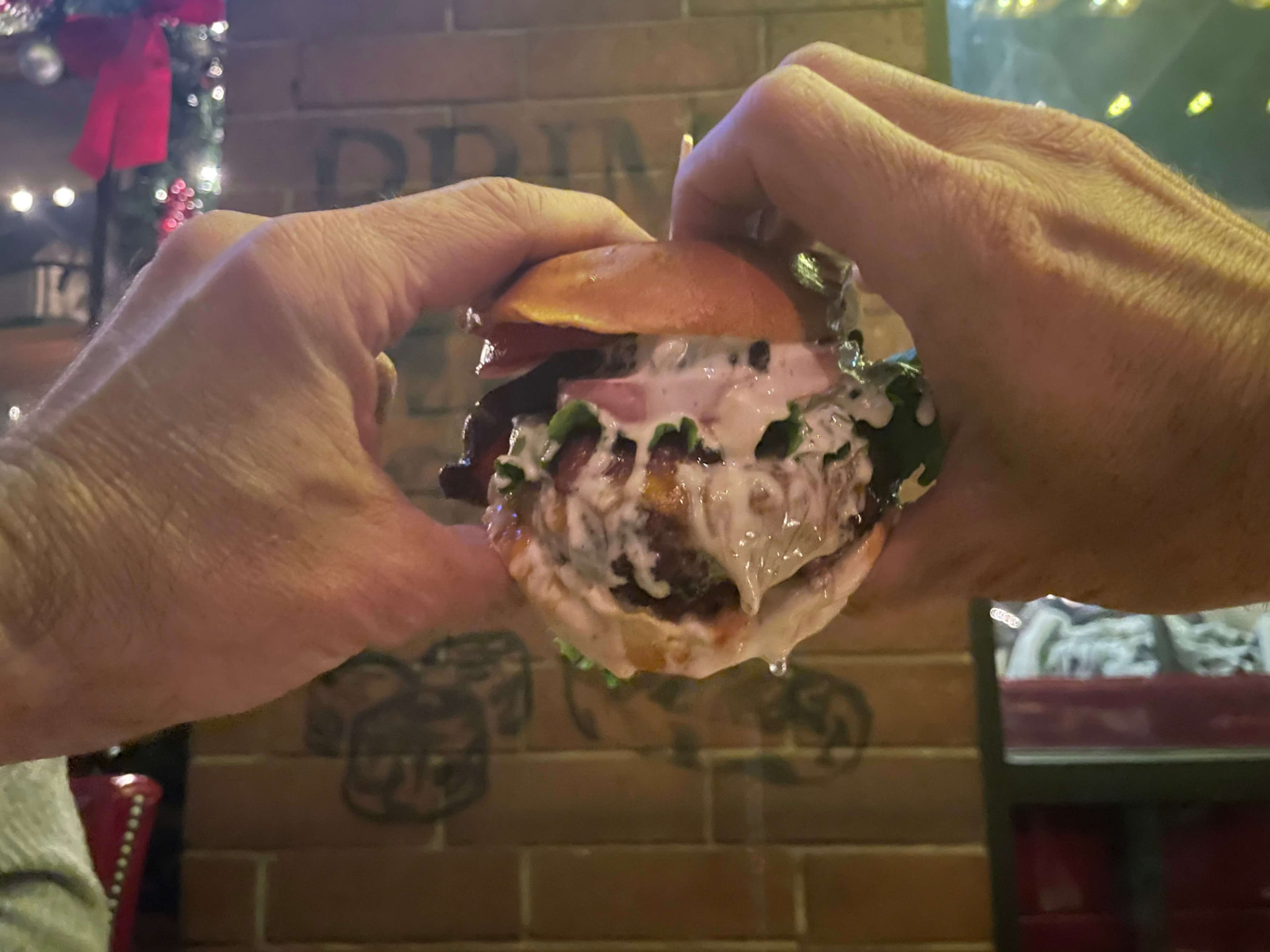 Two hands gripping a saucy burger loaded with Creamy Garlic Foodie Sauce