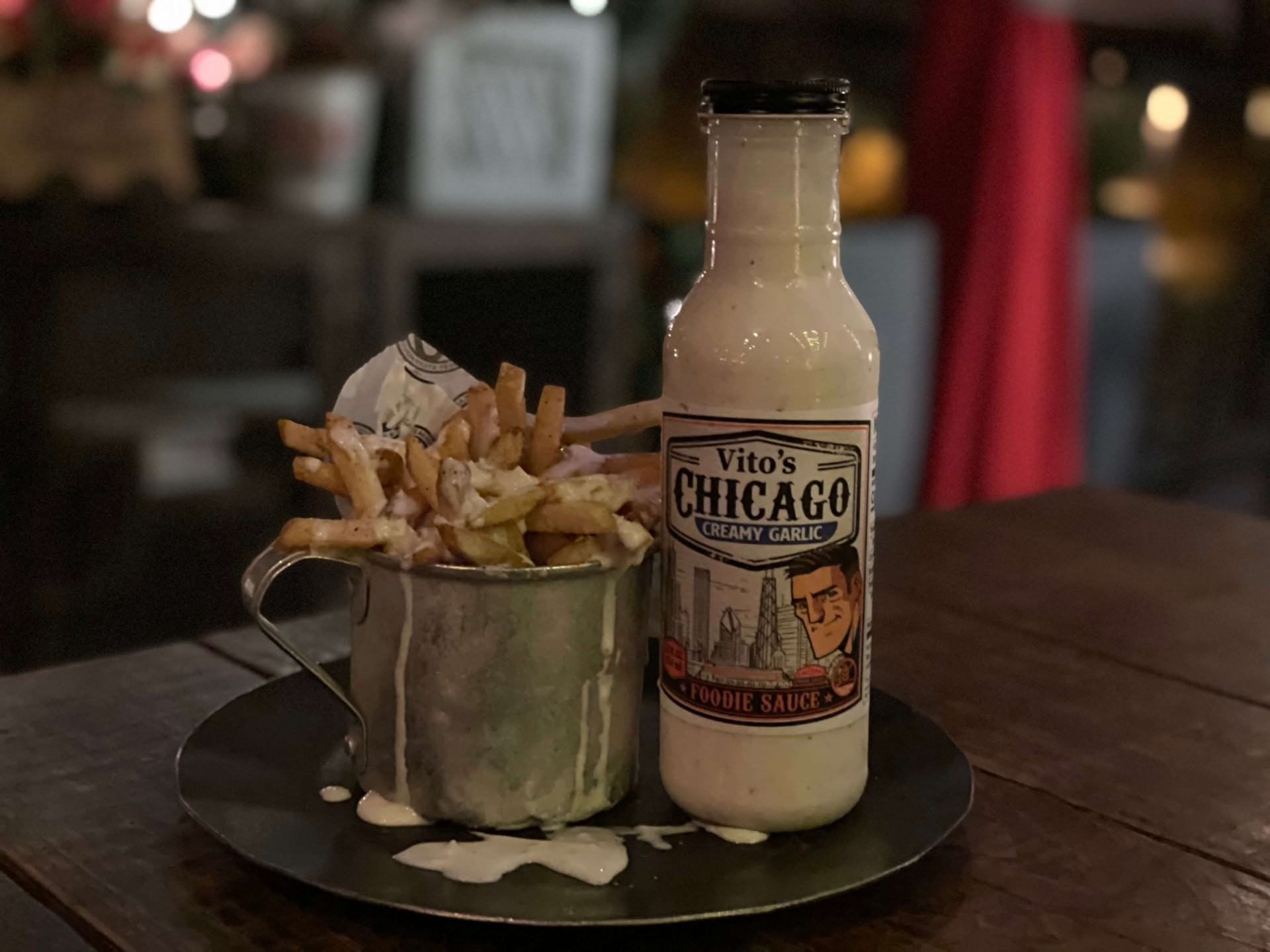 Metal cup of french fries drenched in Creamy Garlic Foodie Sauce next to a bottle on a diner table