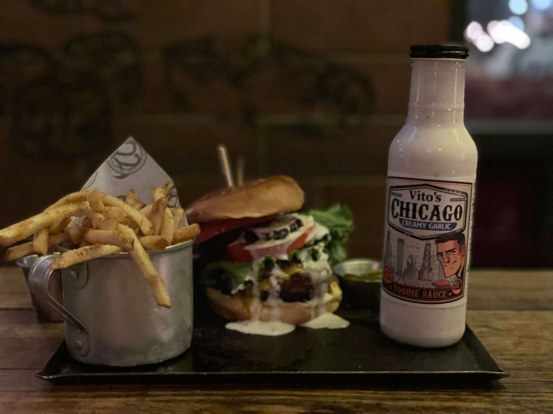 Cheeseburger loaded with Vito's Chicago Creamy Garlic Foodie Sauce beside a basket of fries and a bottle of sauce