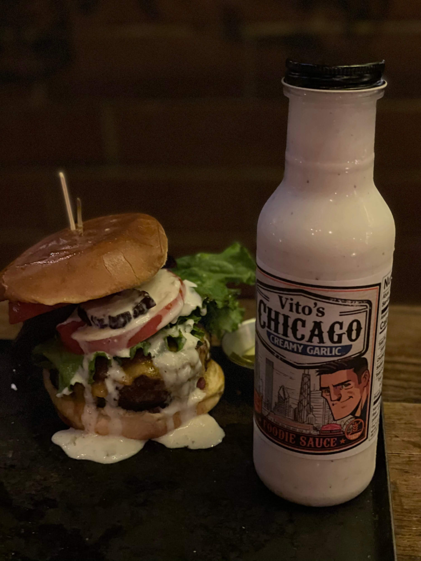 Close-up of a bacon cheeseburger dripping with Creamy Garlic Foodie Sauce beside the bottle